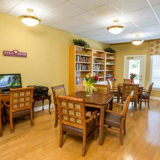 A cozy library room with wooden tables, chairs, bookshelves, and a computer station.