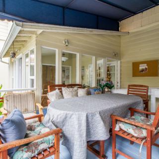 A cozy outdoor patio area with a covered ceiling, featuring a table and cushioned chairs.