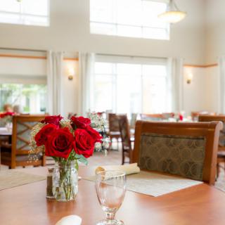 A well-lit dining area with tables set with red roses and chairs.