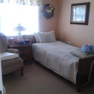 A cozy bedroom with a single bed, armchair, and a side table with a lamp by the window.