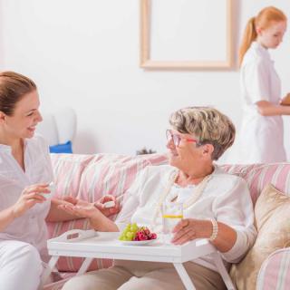 A nurse assists an elderly woman in a home care setting, engaging in a warm conversation.