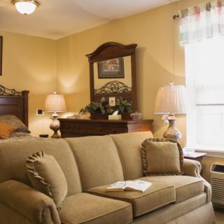 A cozy living room featuring a comfortable sofa, elegant lamps, and classic wooden furniture with a large window allowing natural light.