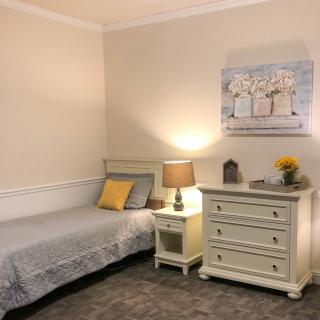 A cozy bedroom featuring a single bed, nightstand, and dresser with warm lighting.