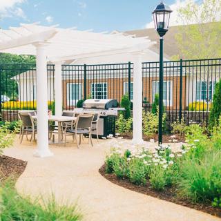 A beautifully landscaped patio area with a pergola, outdoor seating, and a grill.