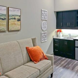 A cozy living area with a beige sofa, orange cushion, and adjacent kitchenette.