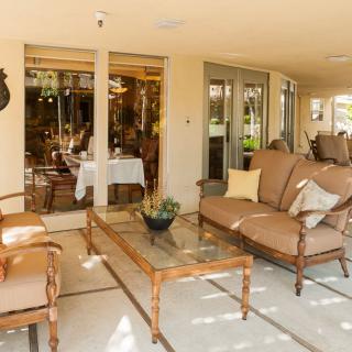 A cozy patio with comfortable outdoor furniture and a glass table, surrounded by lush plants.