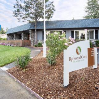 A welcoming entrance to a building surrounded by well-maintained landscaping with a prominent sign in the front.