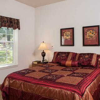 A cozy bedroom with a bed, decorative pillows, artwork on the walls, a lamp, and a window.