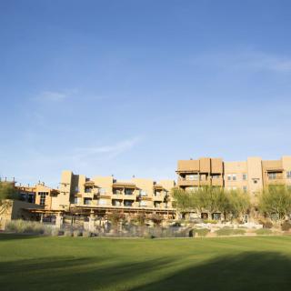 A modern building set against a clear blue sky with a grassy field in the foreground.