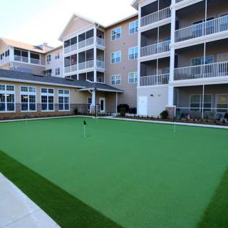 An apartment complex featuring an outdoor putting green surrounded by multi-story buildings with balconies.
