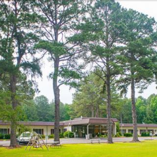 A motel surrounded by tall trees and a well-maintained lawn.