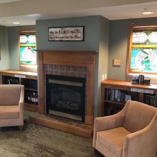 A cozy living room featuring a fireplace, two armchairs, stained glass windows, and built-in bookshelves.