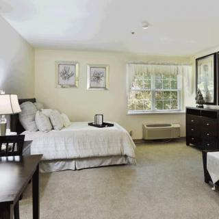 A spacious bedroom with neutral tones, featuring a comfortable bed, dresser, and large window.
