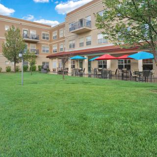 An outdoor view of a residential building with a spacious lawn and patio featuring colorful umbrellas and seating.