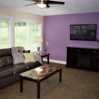 A modern living room with a purple accent wall, sofa, and flat-screen TV.