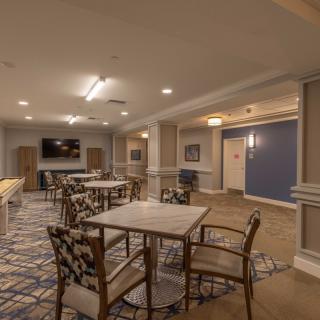 A well-lit dining area with tables and chairs, featuring a television and patterned carpet.