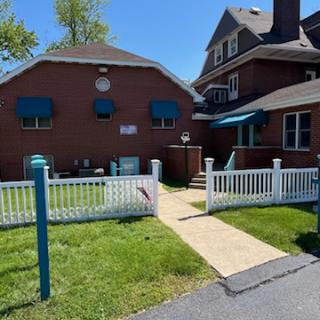 A sunny view of a residential building with a fenced yard and blue awnings.