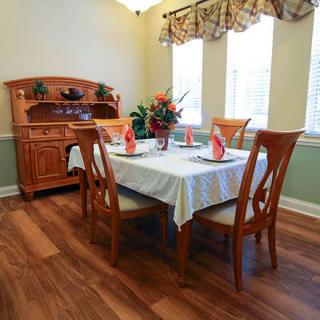 A cozy dining room with a wooden table and chairs, elegantly set for a meal with flowers as a centerpiece.