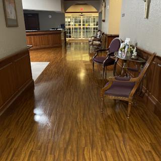 A well-lit hallway featuring wooden flooring and seating arrangements.