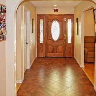 A spacious hallway featuring a wooden front door with glass panels, arched doorways, and tiled flooring.