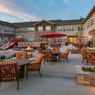 A residential building with a spacious outdoor patio featuring comfortable furniture and a fire pit during the evening.