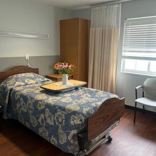 A serene hospital patient room featuring a neatly made bed, a small table with flowers, and natural light coming through the window.