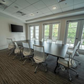 A modern conference room with a large table, surrounding chairs, and a wall-mounted television.