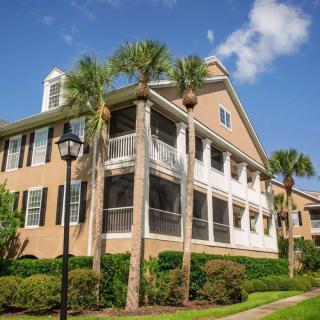 A two-story residential house with screened porches, surrounded by palm trees under a clear blue sky.