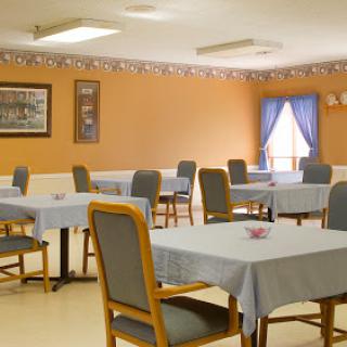 A spacious dining area with neatly arranged tables and chairs, featuring warm orange walls and blue curtains.