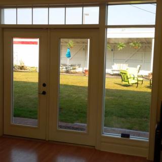 View of a backyard through French doors, featuring a lawn and outdoor furniture.