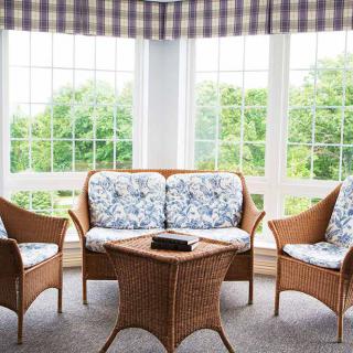 A bright sunroom featuring wicker furniture with floral-patterned cushions and large windows letting in natural light.