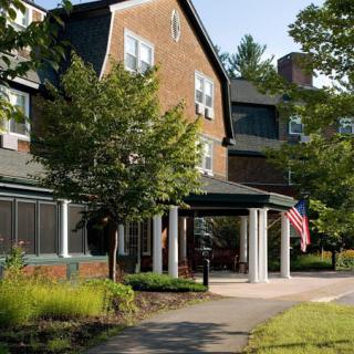 A building facade with an entrance covered by a small porch and an American flag, surrounded by trees and greenery.
