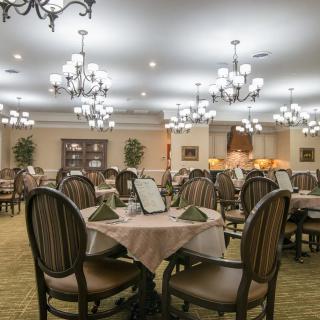 An elegant dining room with tables and chairs arranged under ornate chandeliers.