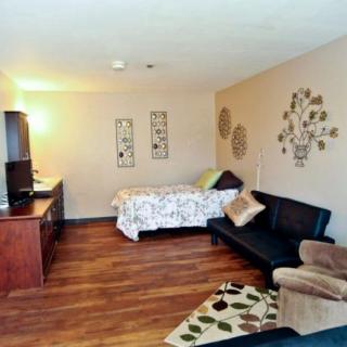 A cozy studio apartment with a bed, couch, and wood flooring.