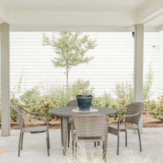 A serene patio setup with a table, chairs, and a potted plant under a covered area, surrounded by lush greenery.