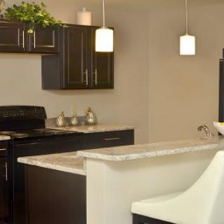A modern kitchen with dark cabinets and a light countertop, featuring pendant lights and a bar stool.