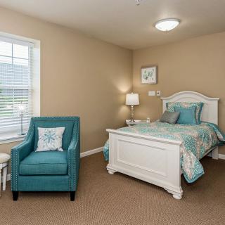 A cozy bedroom with a single bed and an armchair, featuring teal accents.