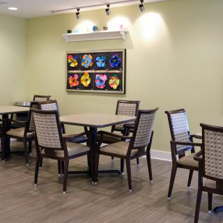 A modern dining room with neatly arranged tables and chairs, adorned by colorful artwork on the wall.