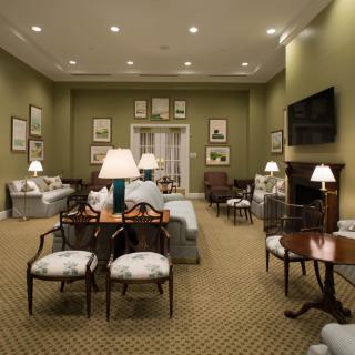 A traditional living room with elegant furniture, including sofas and chairs, softly illuminated by table lamps against a backdrop of framed artwork.