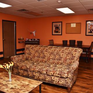 A cozy living room with an orange color scheme featuring a patterned couch, coffee table, and a dining area in the background.