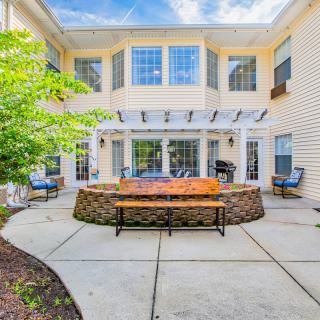 A cozy residential backyard patio with benches, a pergola, and landscaped surroundings.
