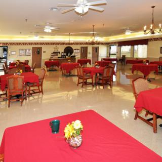 A spacious indoor dining area featuring tables with red tablecloths and decorated with flowers.