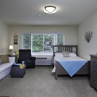 A cozy bedroom with a bed, sofa, chair, and large window view.
