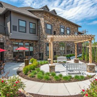 A beautifully landscaped backyard with a pergola and outdoor seating area, adjacent to a residential building.
