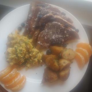 A plate with a meal consisting of meat, potatoes, scrambled eggs, and orange slices.