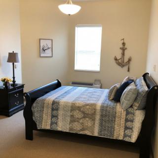 A cozy bedroom with nautical-themed decor, featuring a double bed, nightstand with a lamp, and an anchor wall hanging.