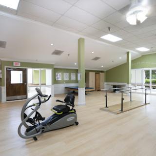A bright and spacious rehabilitation gym featuring an elliptical machine and parallel bars for physical therapy.