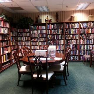 A cozy library corner with shelves filled with books and a round table surrounded by chairs.