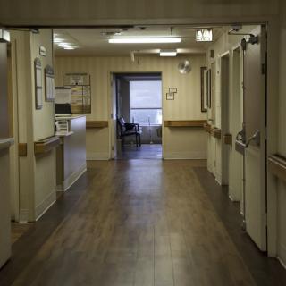 An empty hospital hallway with multiple doors and a window at the end.