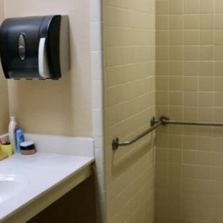A bathroom with a sink, paper towel dispenser, and a tiled shower area with a handrail.